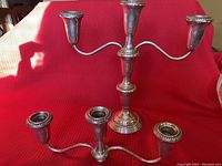 Front view of assembled 3-arm sterling silver weighted candelabra and separate candle holders in front on red background.