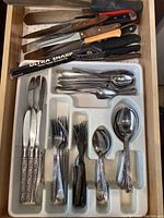 Assorted flatware and cutlery knives in a drawer and plastic utensil tray