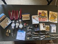 Wide view showing all items displayed on black surface, including knives, watches, tie pins, buttons, and stickers.