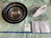 Hamilton Beach white hand mixer with wire whisk and two beaters, instruction manual, and a ruler for scale, along with a small box labeled Expert Owls
