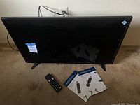 The Insignia 33-inch TV resting on a carpeted floor with its remote control and two manuals placed in front.