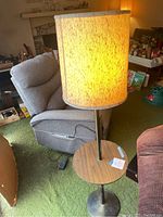 Floor lamp with laminate wood table, brass pole, round metal base, and fabric lampshade illuminated in a living room setting.
