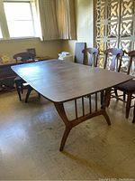 Dining table shown fitted with one leaf, six chairs positioned behind, room background.