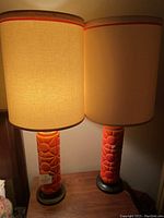 Pair of lit orange vintage midcentury lamps on wooden side table with visible glow through lampshades showing warm light effect