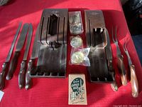 Two Cutco cutlery sets with original brown plastic trays and several knives and forks, plus vintage candle holder items in original packaging and a small original candle vase box on a red surface.