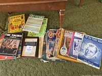 Full view of various vintage music books and sheet music arranged on a carpet, showing multiple titles and colorful, illustrated covers.