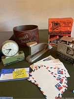 Photo showing full lot contents from an angle. Items include Wesclox clock, postal scale, mail bucket, Ace Scout stapler with box, envelopes and label sheets clearly visible.