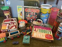 Overview photo of the full lots contents spread on carpet showing Fisher-Price train, chatter phone, radio, Lego, Tiddlywinks game, Charlie Brown projector/viewer, and other vintage toys and games.