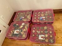 Seven red plastic containers with transparent lids showing various gold, bronze, and glittery Christmas ornaments and decorations inside.