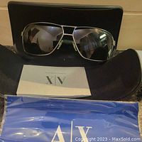 Front view of sunglasses with case, cloth, and booklet in background