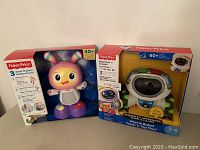Two Fisher Price baby toys in original packaging, one Teach 'n Tag Movi robot for ages 3-6 and one colorful infant dancing toy for 6 months+. Both new in box.