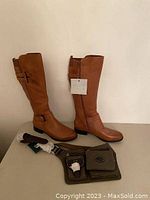 Full view of a pair of brown leather boots with buckle details and a green canvas belt bag with compartments and accessories on a surface.