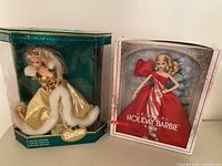 Photo of two boxed Holiday Barbie dolls: one in gold fur-trimmed gown and one in red bow dress