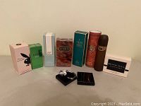 View of all 8 assorted colognes in original boxes, arranged in a row with one smaller decorative item