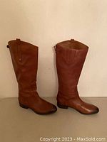 Side view of both new brown leather boots showing the full height and shape.