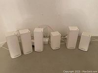 Front view showing six white Linksys WiFi signal boosters lined up with cables.