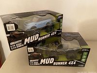 Two boxed Mud Runner 1:14 scale 4x4 remote control trucks with visible packaging and branding.
