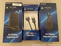 Front view of three boxed Sony PS Vita charging accessories - AC adaptor, USB cable, car adaptor.