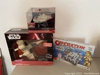 Photo showing all three boxed items: Millennium Falcon alarm clock on top, remote control X-Wing plane at bottom left, and Operation Star Wars board game on right.