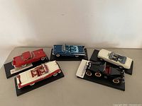 Five vintage die cast model cars arranged in a row on black display bases with labels, showing their various colors and designs.