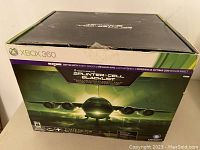 Closed green and black retail box featuring Xbox 360 logo and Tom Clancy's Splinter Cell Blacklist branding.