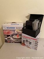 Zojirushi Gourmet Electric Skillet in box, Lagostina Ticino Multi-Cooker box with black gift box on top