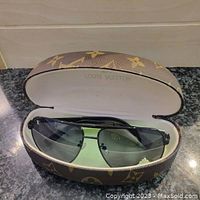 Sunglasses inside the open Louis Vuitton monogram hard case showing front view of glasses and interior brand imprint.