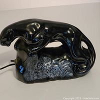 Front-left angled photo showing the panther lamp's full shape and detailed glossy black ceramic finish.