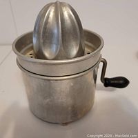 View of vintage manual juicer showing metal reamer cone, strainer, and container with hand crank handle.