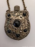 Front view of antique small perfume bottle pendant showing detailed metalwork and five small black stones with one large central black stone.