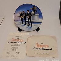 Photo showing Delphi collectible plate featuring The Beatles performing live, displayed on a stand, accompanied by certificate and packaging.