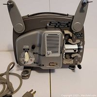 Side view of Bolex Paillard 8mm film projector showing power knob, manual threading wheel, lens focus adjustment and power cord.