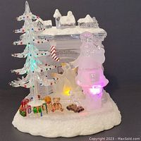 Front view of light-up Santa Christmas decoration with fireplace, tree, presents, teddy bear, and reindeer on snowy base.