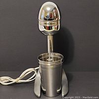 Side view of Hamilton Beach Salton Drink Mixer with chrome top and stainless steel cup, black plastic base sides visible, with attached power cord.