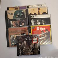 Front view of the nine Beatles CDs showing album cover art including the 'Let It Be' and 'With the Beatles' albums.