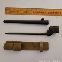 Top view of the bayonet, metal cover, and belt case aligned next to a measuring ruler showing dimensions.