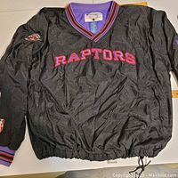 Front view of black Raptors wind breaker jacket showing Raptors text and team logo patch on sleeve