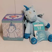 Light blue unicorn plush with metallic blue horn, wings, and hooves next to the themed box and scent packet.