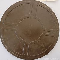 Top view of round metal 16mm film reel tin in dark brown with worn surface and embossed logo on lid.