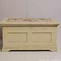 Front view of rectangular wooden cream-colored storage box showing paneled sides and raised base.