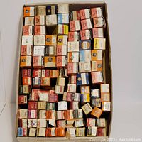 Top view of a box filled with numerous vacuum tube boxes from brands like GE, RCA, Standard Brand, with various colors including orange, white, and black. Tubes are stored in their original boxes, tightly packed.