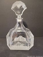 Full clear lead crystal decanter with frosted ornate detailing and stopper shown upright against a dark background.