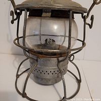 Side view of vintage Adlake kerosene lantern showing intact clear glass globe and metal wire protective cage over the burner and base.
