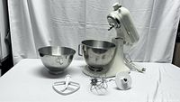 Full view of Cuisinart stand mixer base with two stainless steel bowls and three attachments laid out in front on white background