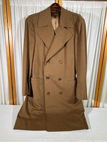 Full front view of brown long double breasted coat on hanger with visible buttons and pockets.