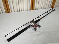 Full view of the fishing rod and reel together showing black rod with foam handle and attached red and silver reel.