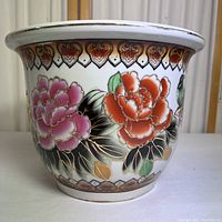 Front side of ceramic flower pot showing vibrant pink and red flowers with leaves and decorative border pattern on the rim.