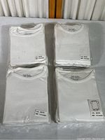 Four packages of white baby onesies, each package containing five onesies, sealed in clear plastic with size and color labels visible.