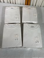 Four packs of white children's T-shirts, each pack containing 5 T-shirts, with one package partially opened for display.