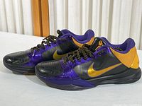 Side angle showing both Nike Zoom Kobe 4 shoes with purple, gold, and black colors on a flat surface.